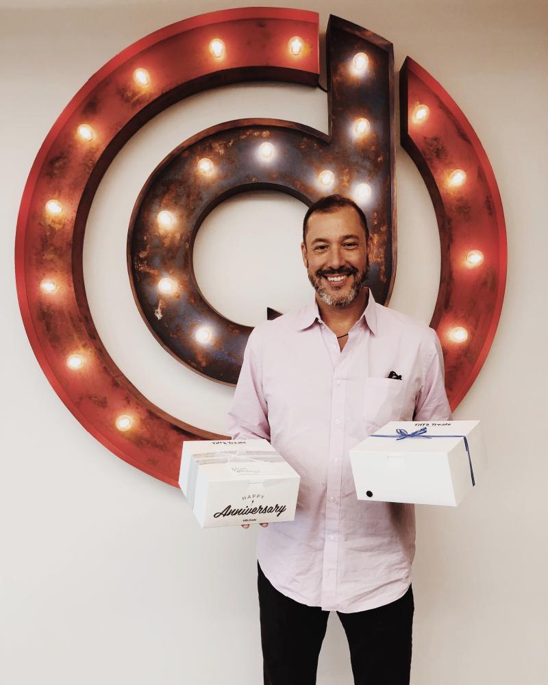 Sean Spector holding anniversary boxes in front of an illuminated Dropoff sign