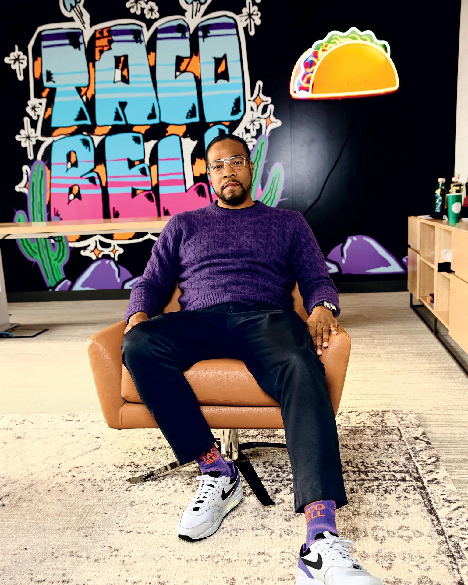 Sean Tresvant seated in a Taco Bell office in front of a colorful mural and neon taco sign