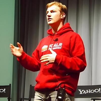 Sebastian Stadil speaking in a red Scalr hoodie, with his hands raised as he explains a point.