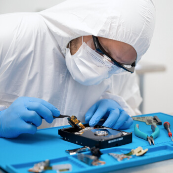 A technician in protective clothing works on an open hard drive in a recovery laboratory
