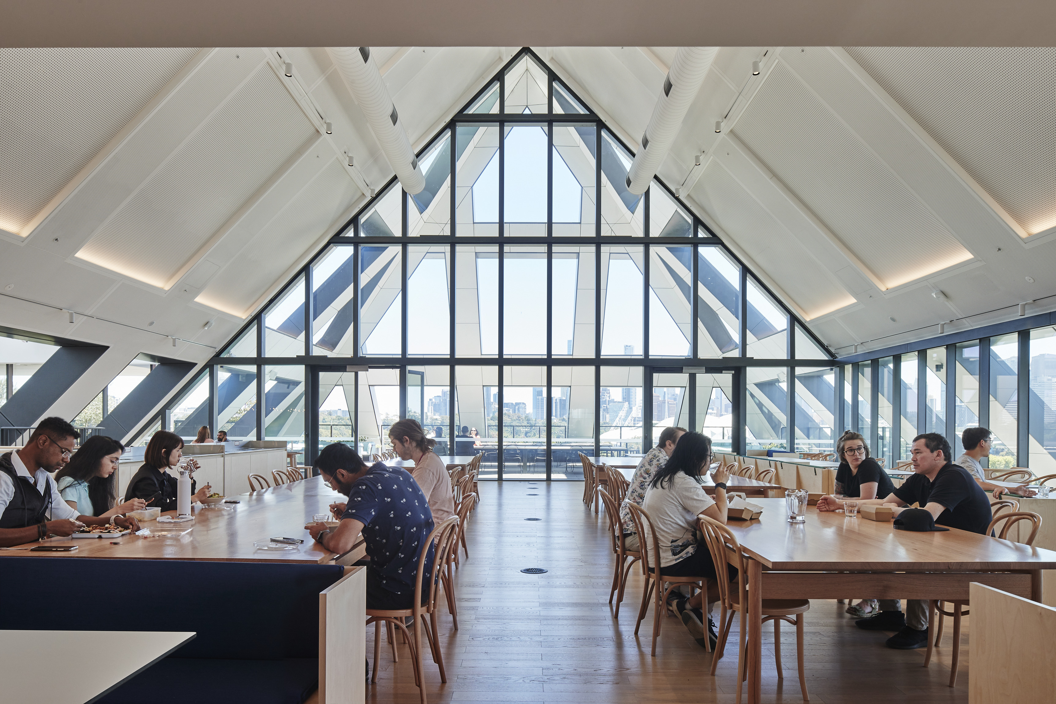 People eat and talk at long tables beneath the gabled roof of SEEK’s headquarters.