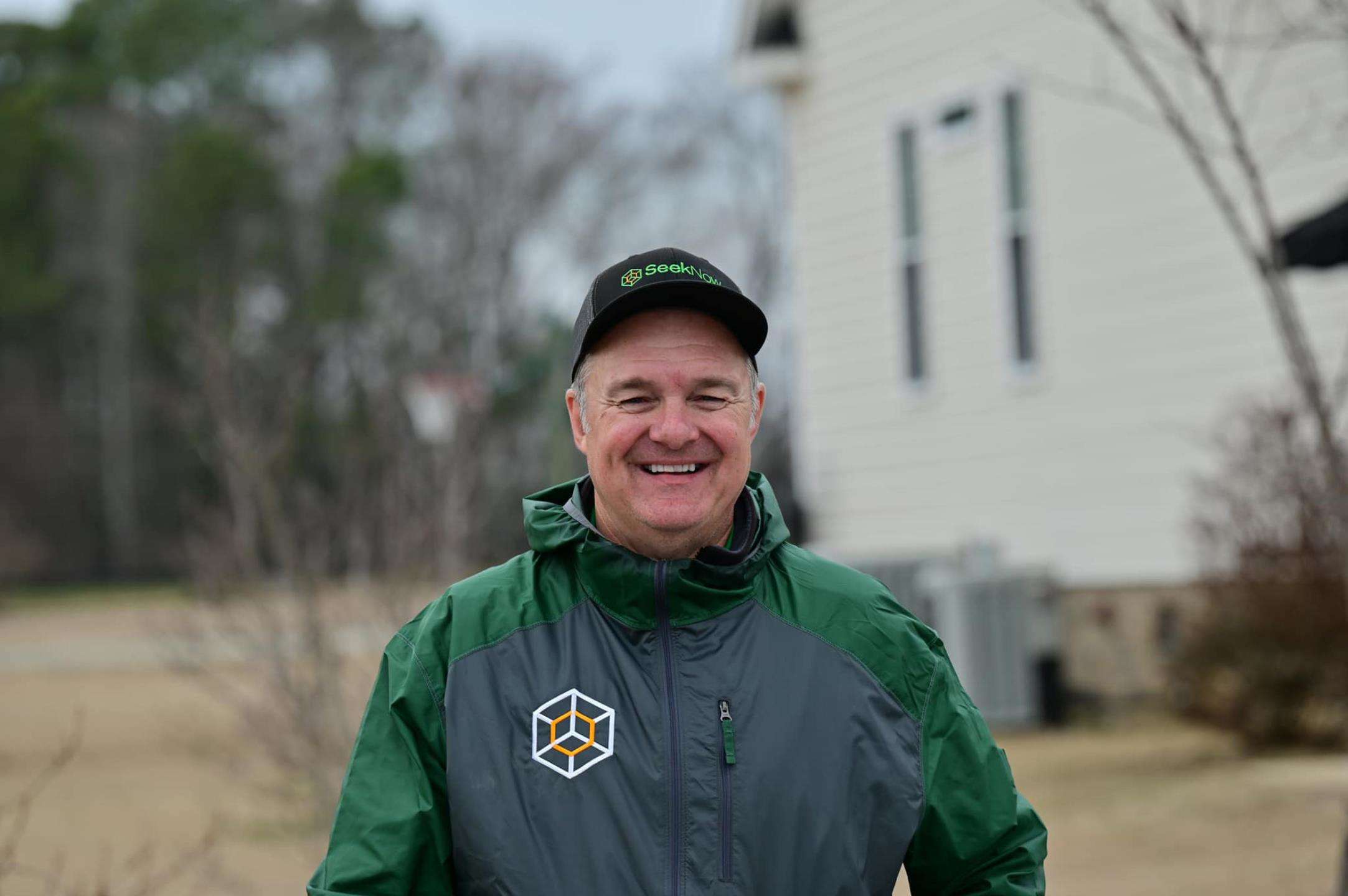 A Seek Now representative wearing a branded cap and green jacket outside a residential property