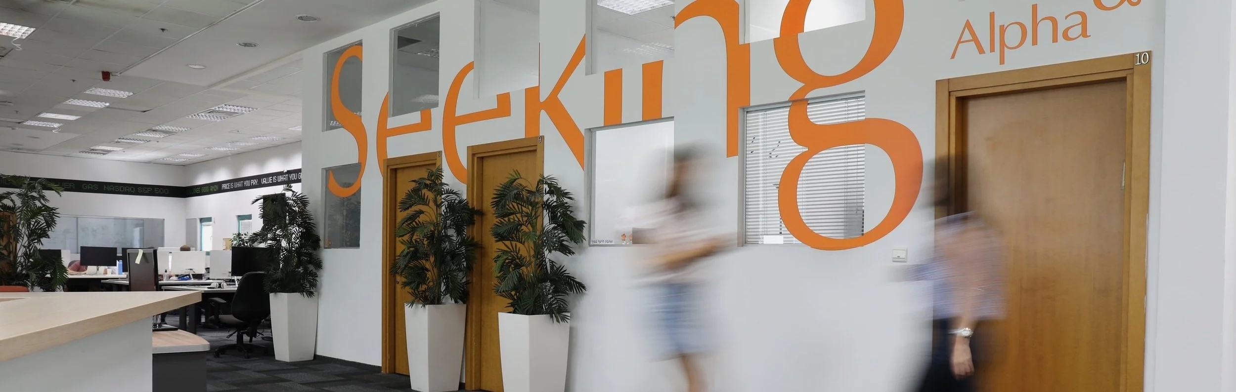 Seeking Alpha office with orange lettering, desks, and people walking past
