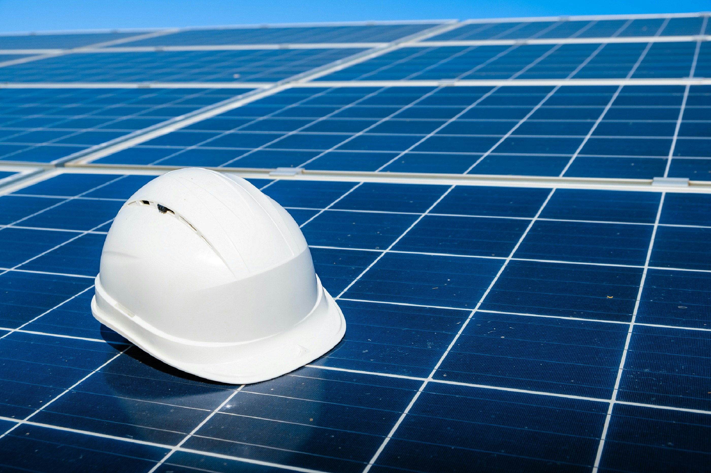 A hard hat resting on a utility-scale solar panel under a blue sky