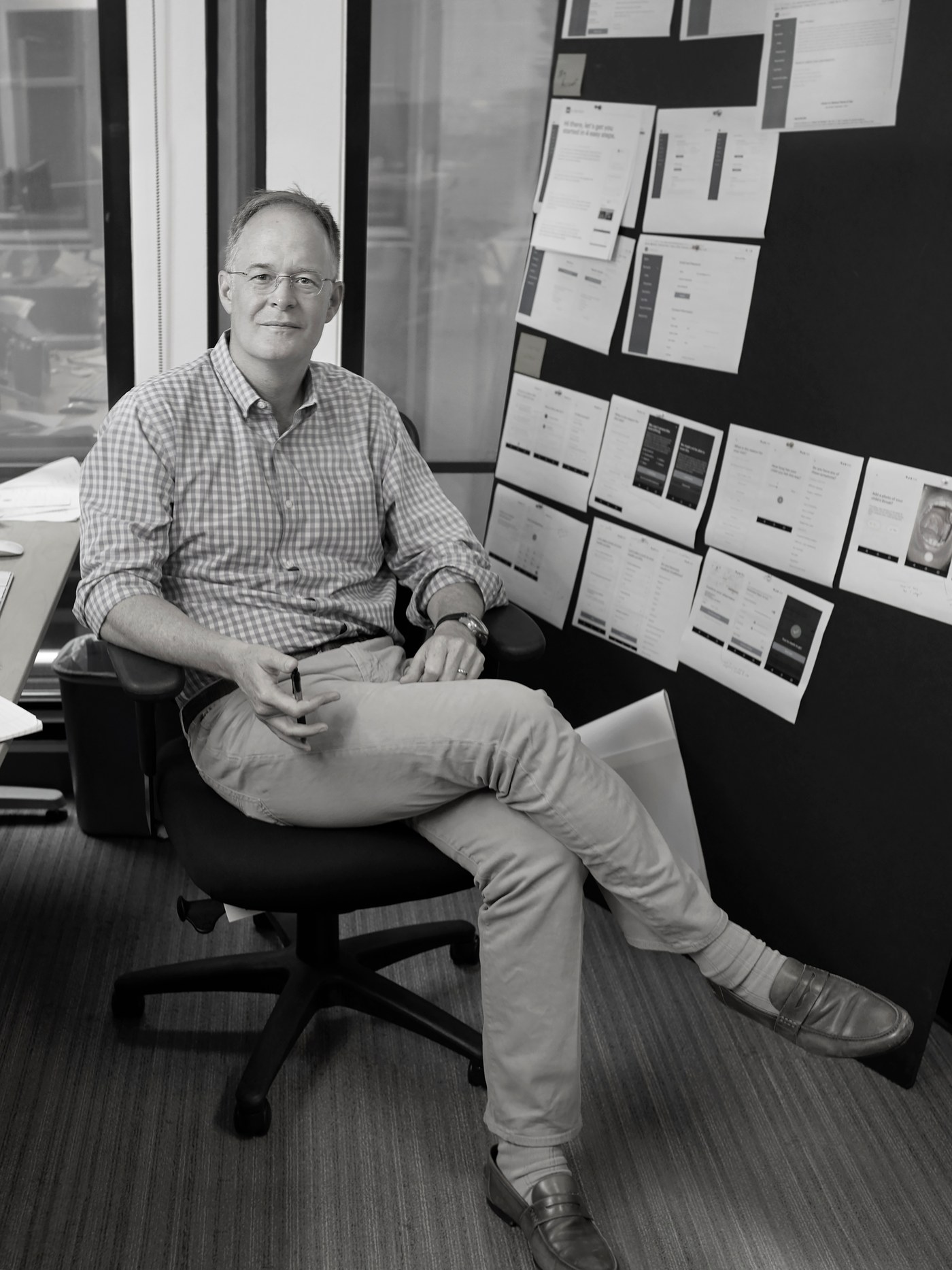 A product leader seated beside a wall of printed HR interface designs