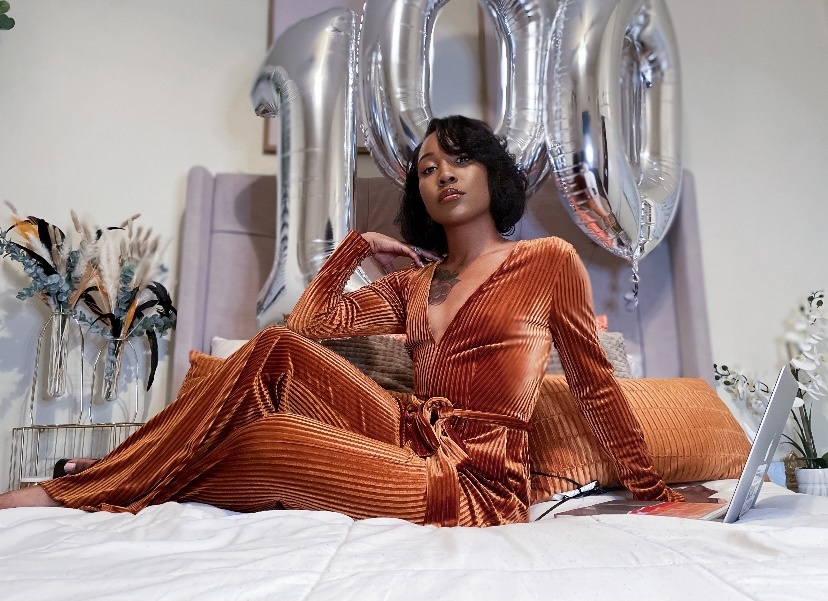 Nia Rice seated in an orange outfit, with silver balloons behind her