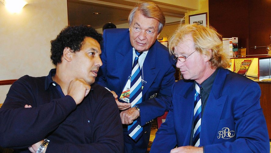 Serge Kampf leaning forward in conversation with Serge Blanco and Jean-Pierre Rives
