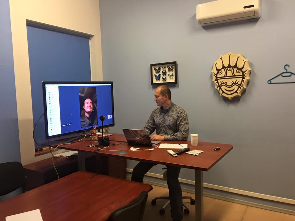 Rizhikov at an adjustable desk with a colleague visible on a large screen