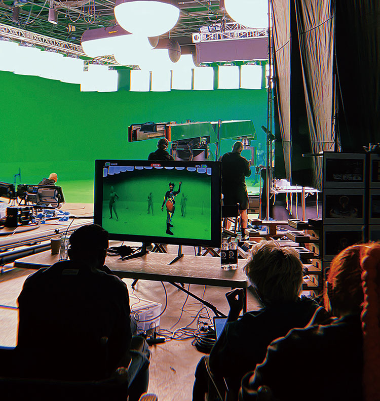 An AMAZE concert production on a green-screen stage, with crew members watching a performance monitor