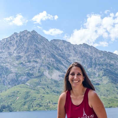 Shannan Carr smiling outdoors, with mountains and water behind her.