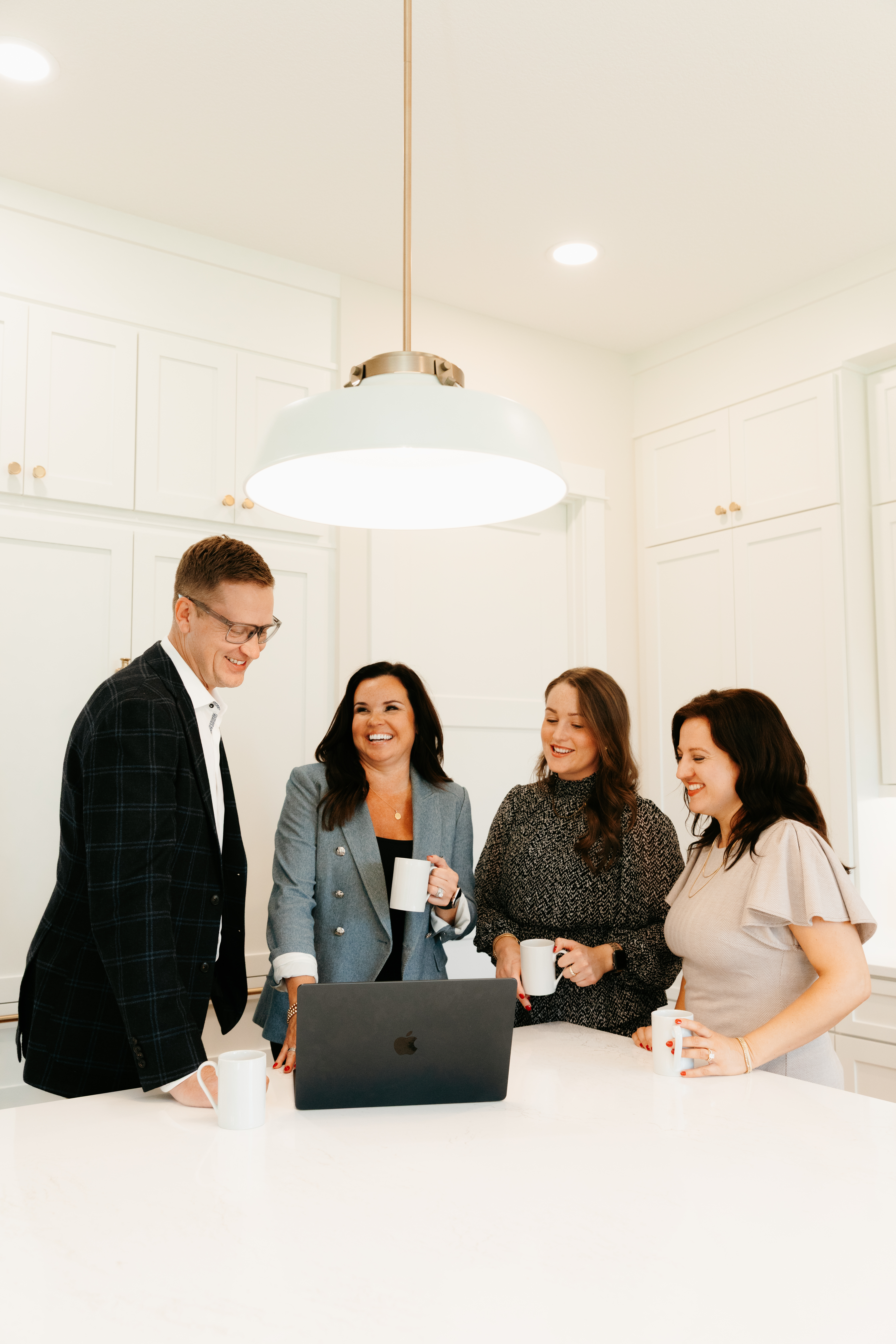 Four Brooks Team members gathered around a laptop with coffee mugs in a bright kitchen