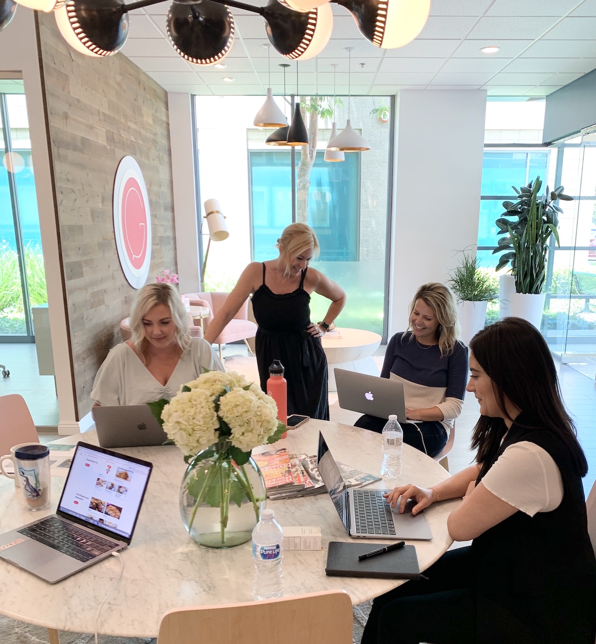 Four GOLD PR team members working around a table with laptops in a bright office