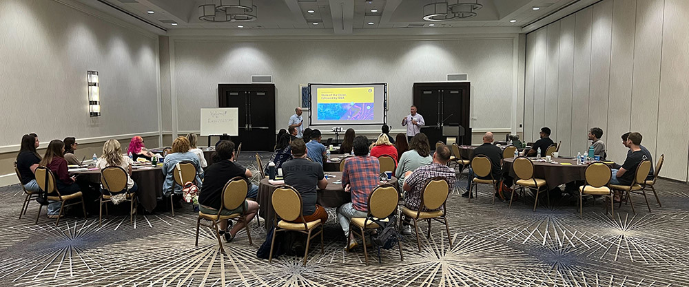 Shawn Rubel and Adam Gamble presenting to Vecteezy colleagues seated around tables in Orlando