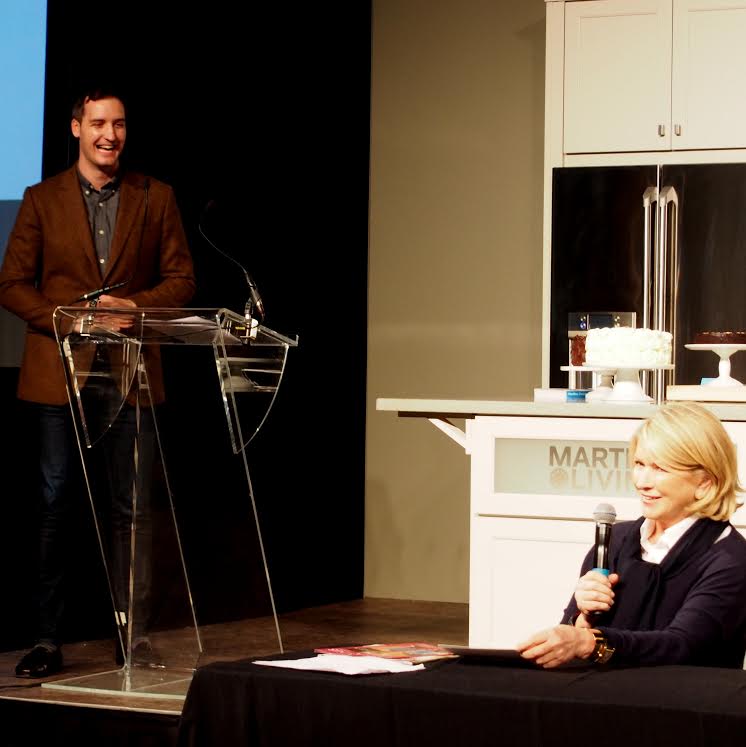 Shawn Rusich at a lectern introducing Martha Stewart, who is seated with a microphone at the Delicious Food Show.