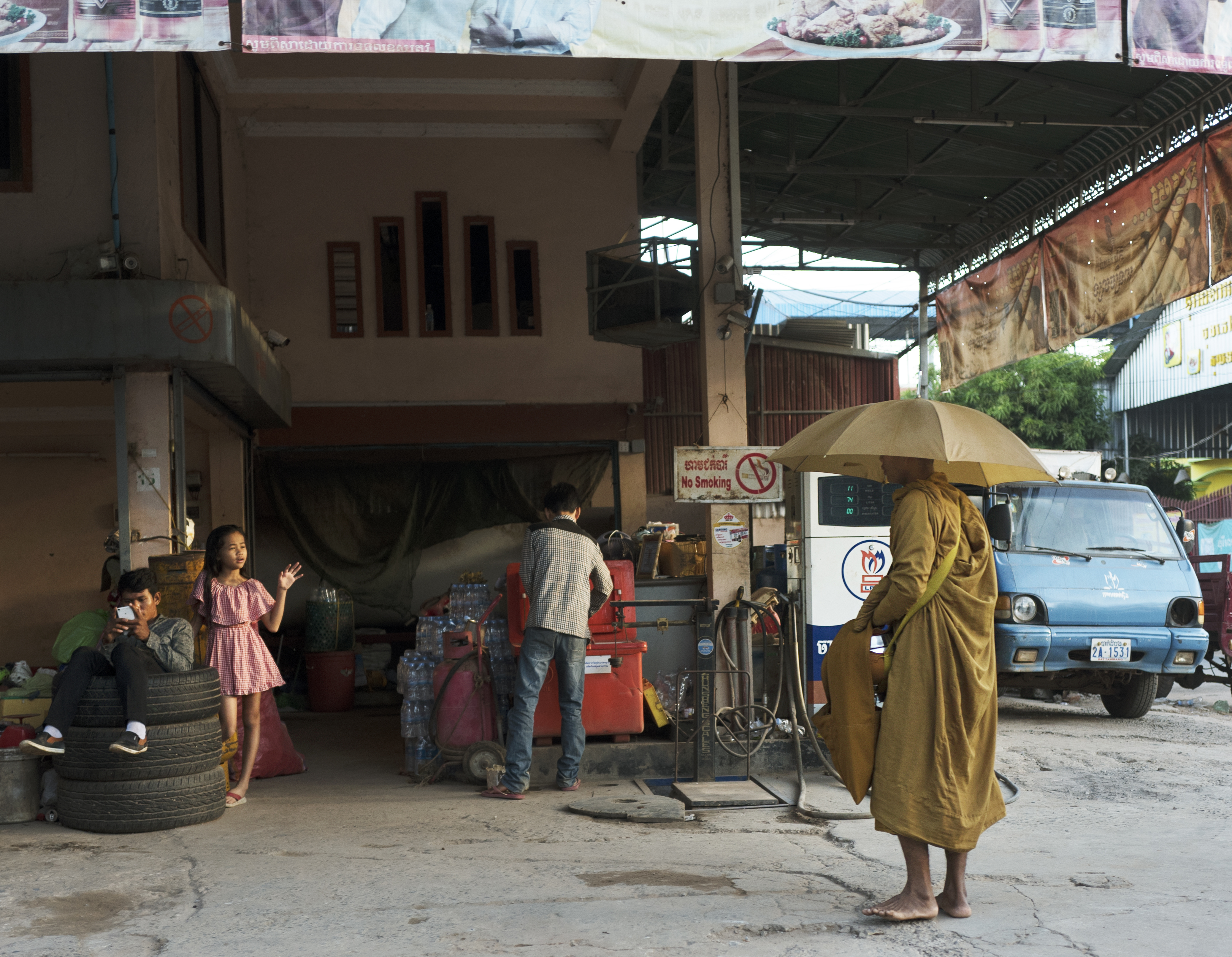 A travel photograph by Shawn Sachs showing a street scene, people, an umbrella and a blue vehicle