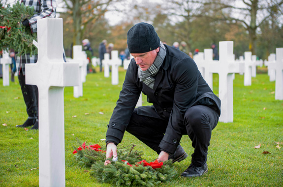 Shawn Stewart kneels to place a wreath beside a white cemetery marker
