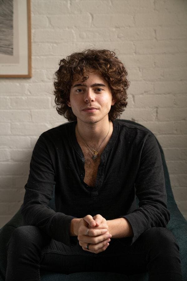 Shayne Coplan seated at work in 2020, in front of a white brick wall
