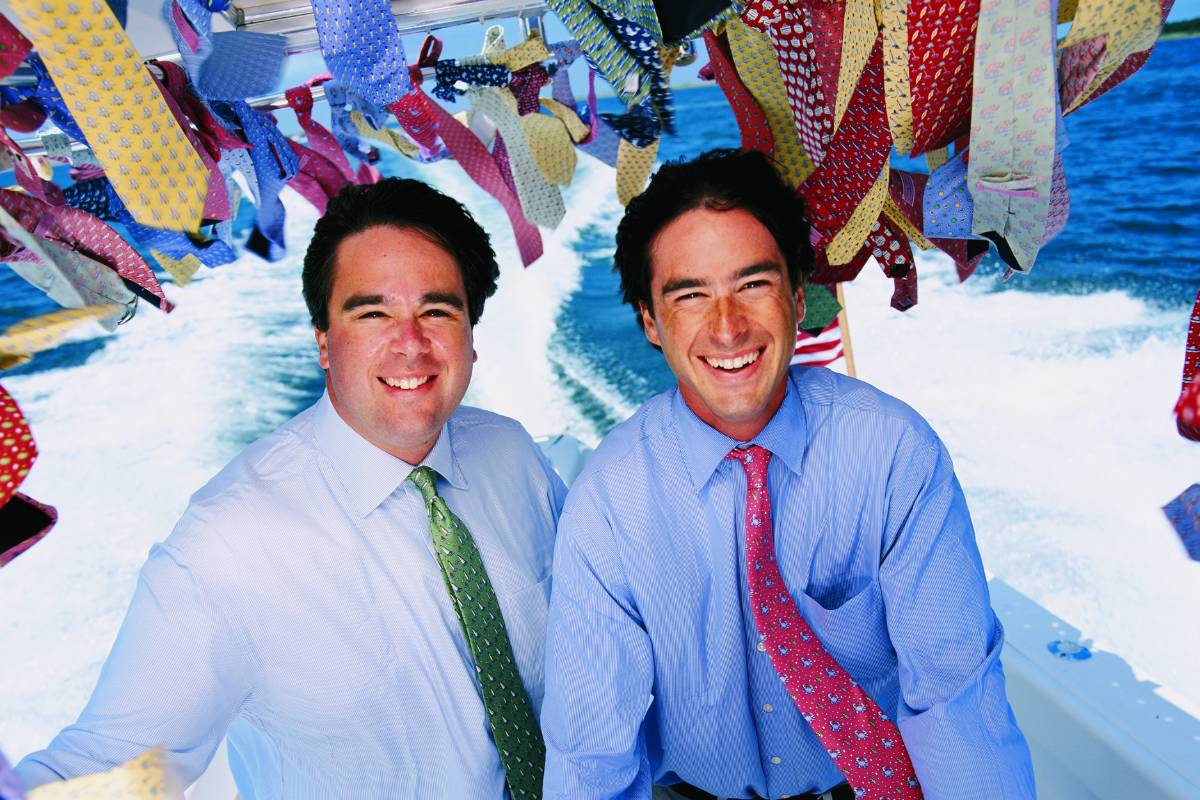 Shep and Ian Murray aboard a boat with colorful ties hanging overhead