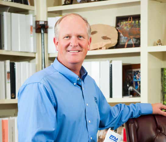 Sherman Miller in a blue shirt standing beside a chair in an office with shelves of binders