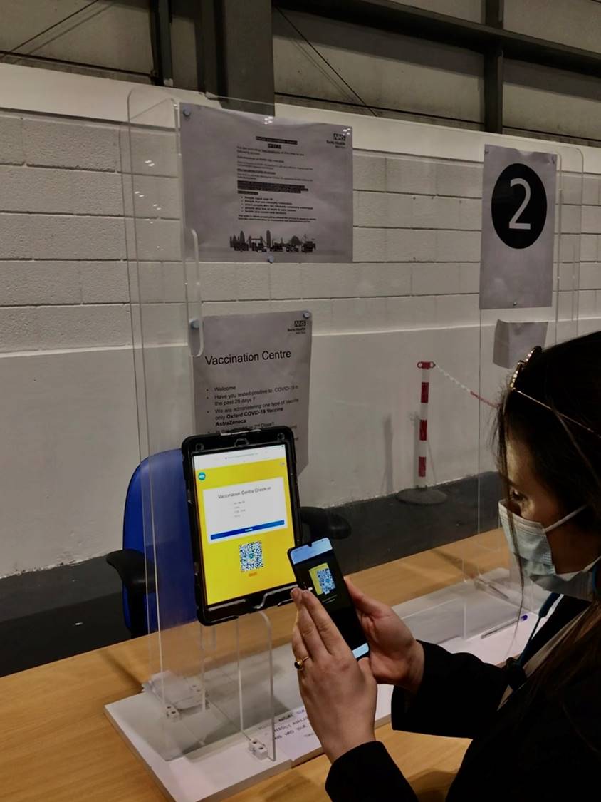 A masked person scans a CATQR check-in code with a phone at the ExCeL vaccination centre.