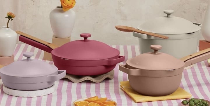 Our Place cookware in pink, cream and lilac on a striped tablecloth