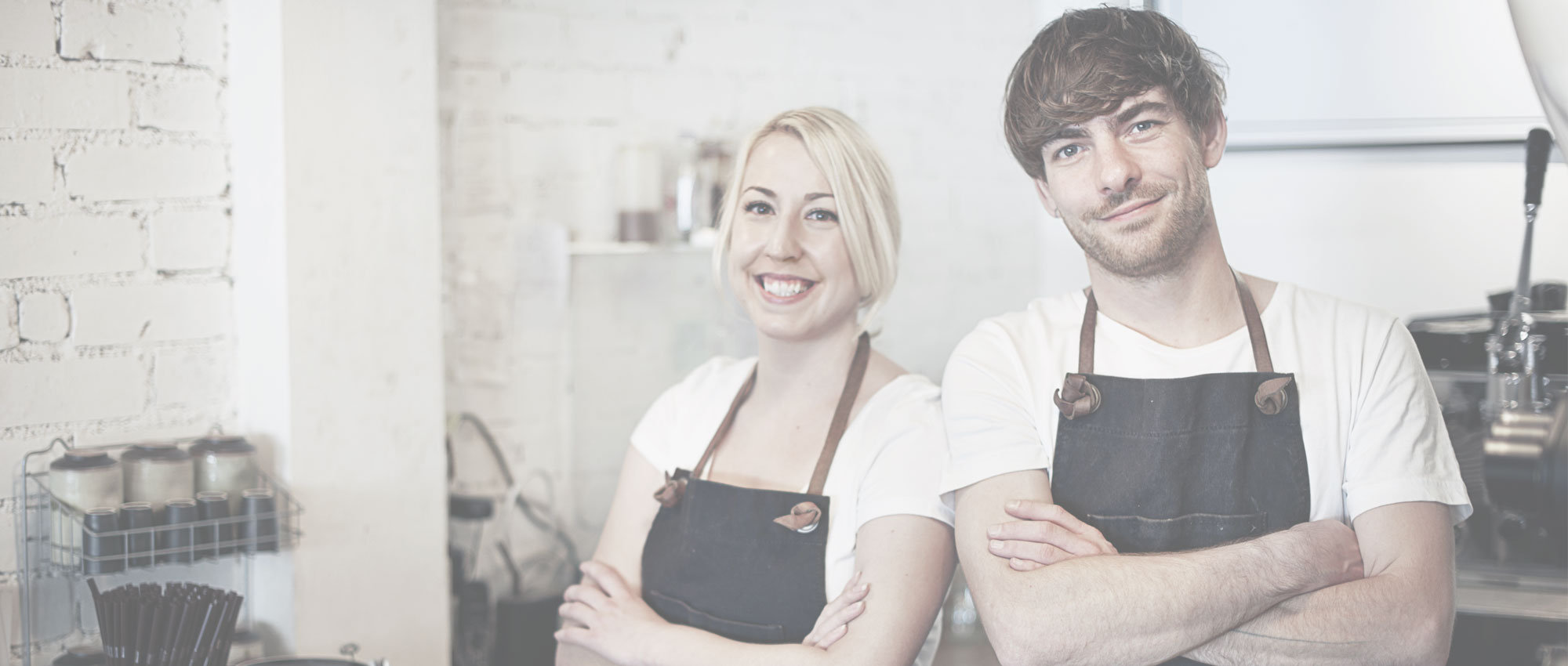 Two small-business owners in aprons standing in their shop