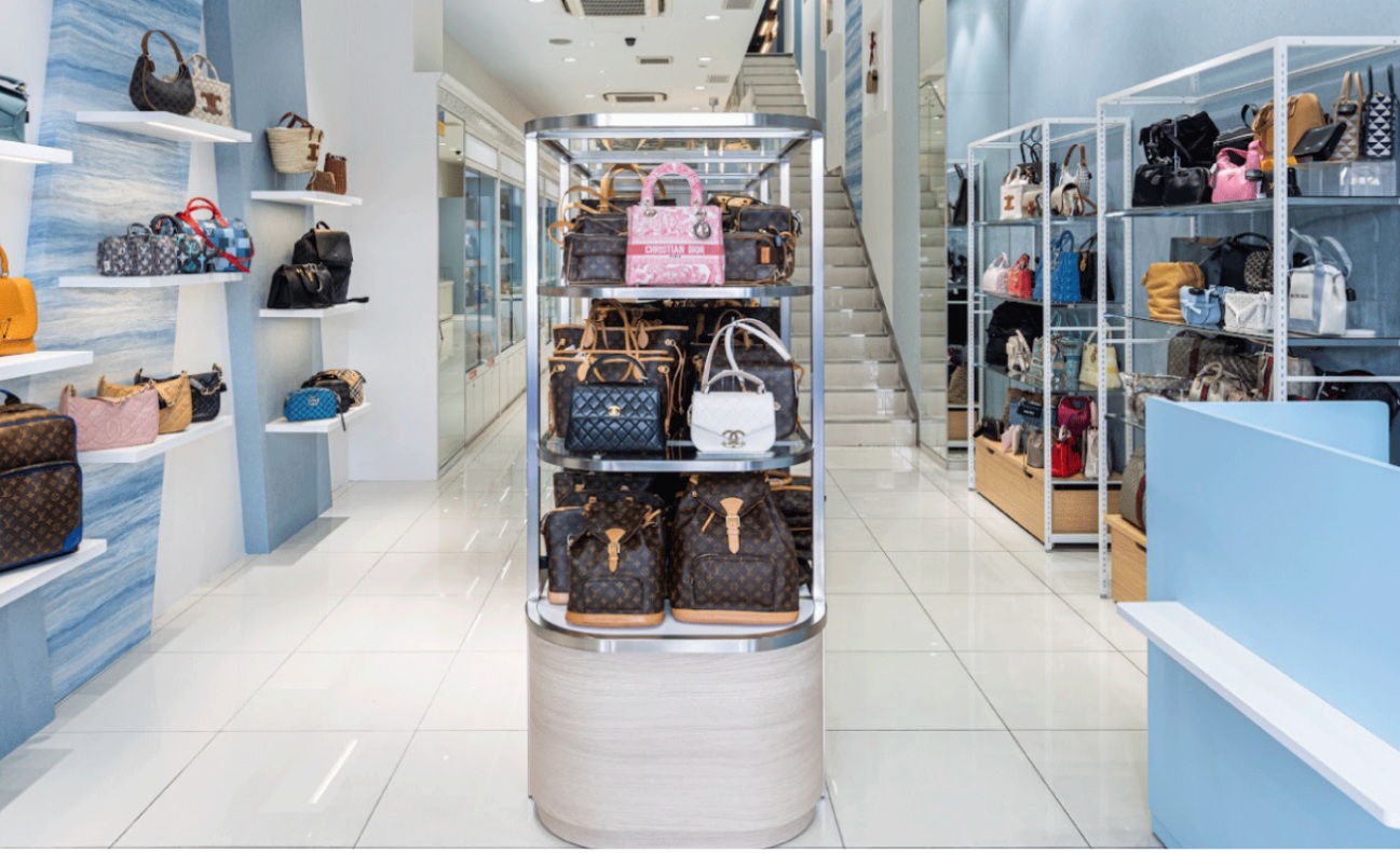 Designer handbags displayed on shelves and a central stand in a luxury resale boutique