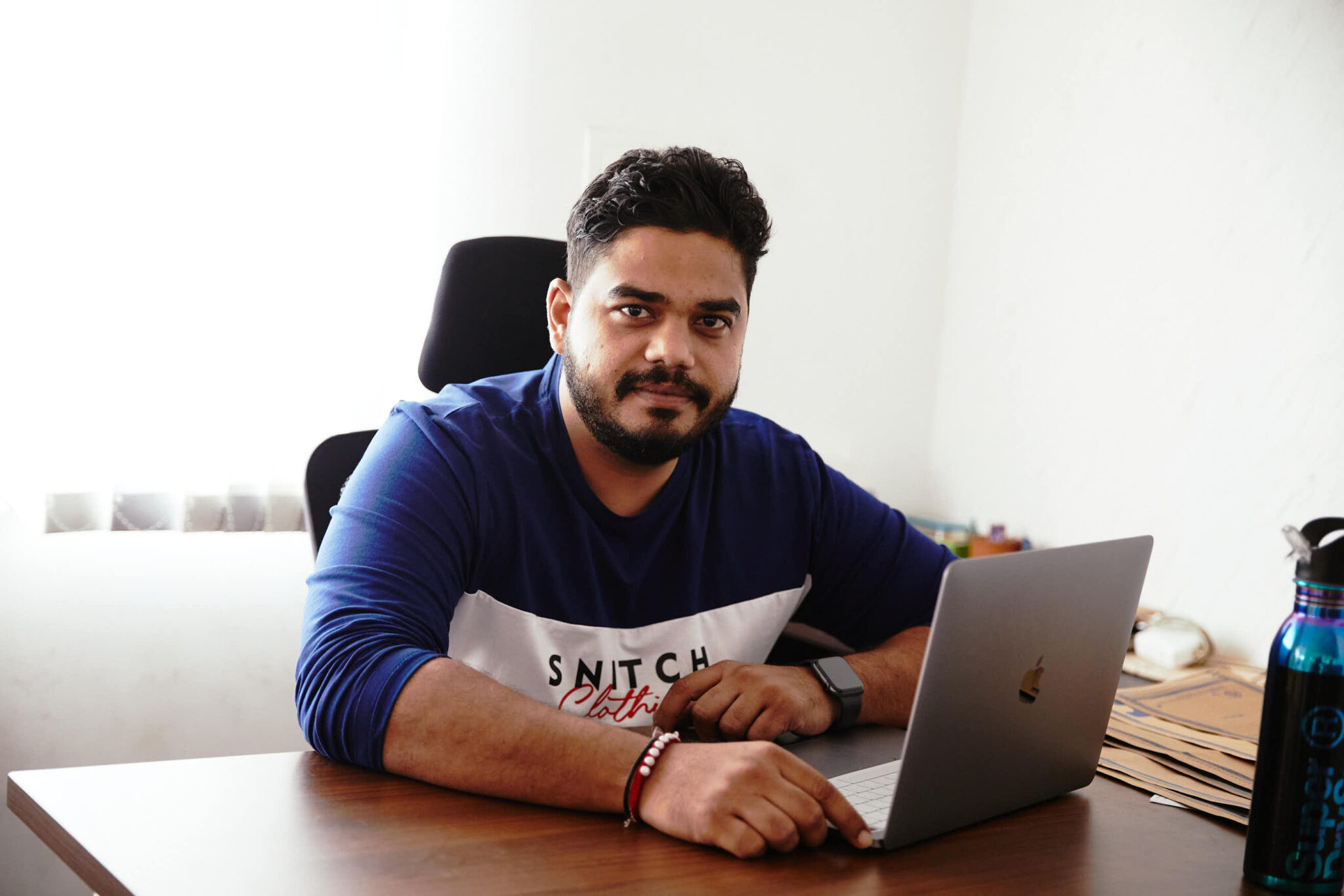 Siddharth Dungarwal seated at his office desk, wearing a Snitch shirt beside an open laptop