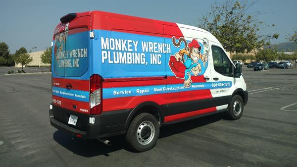 Monkey Wrench Plumbing van with red and turquoise graphics and a cartoon mascot