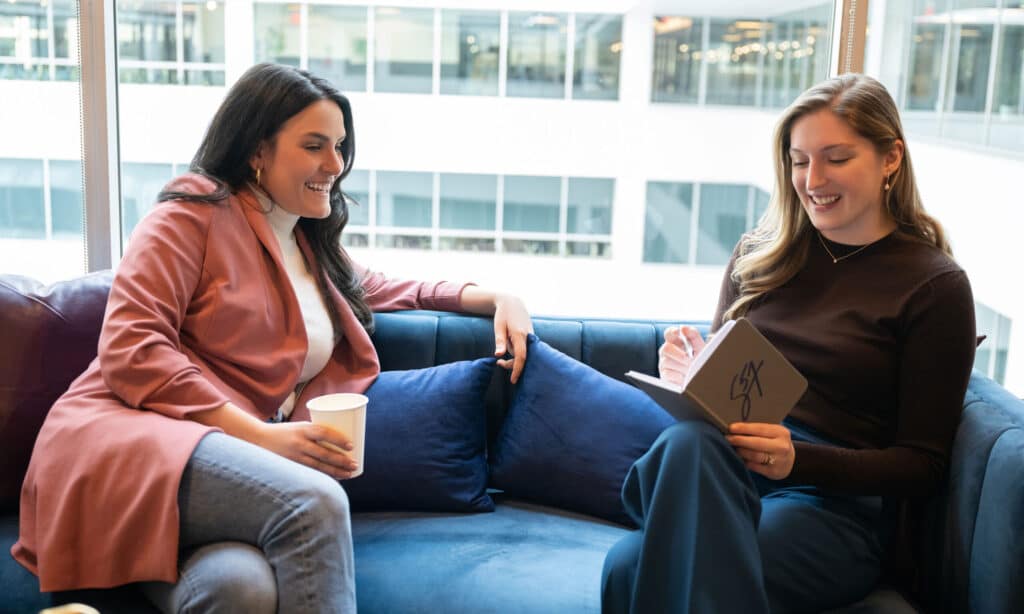 Two Signature 57 colleagues talk while one writes in a notebook