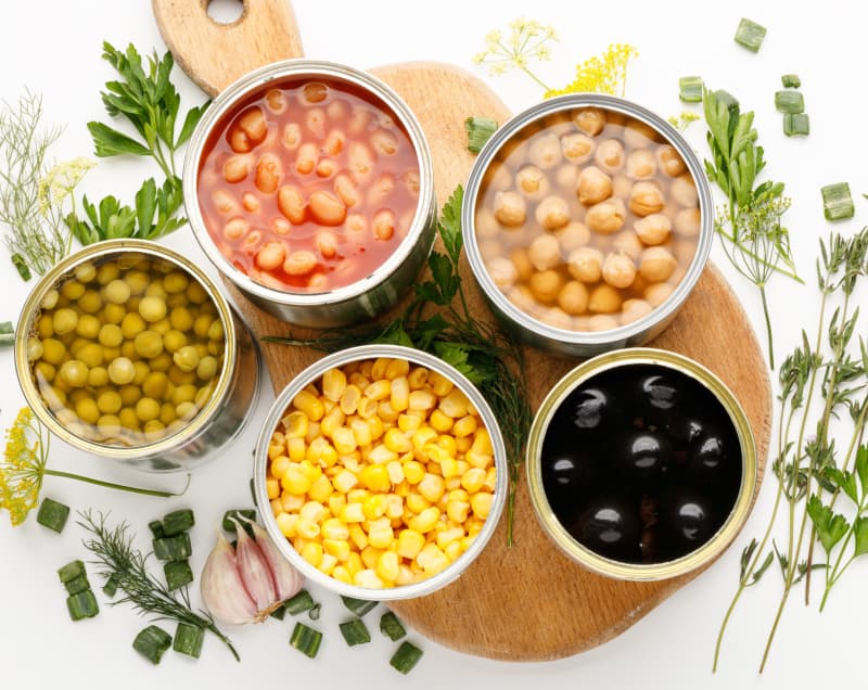 Opened food cans containing peas, corn, chickpeas, beans and tomato-based food