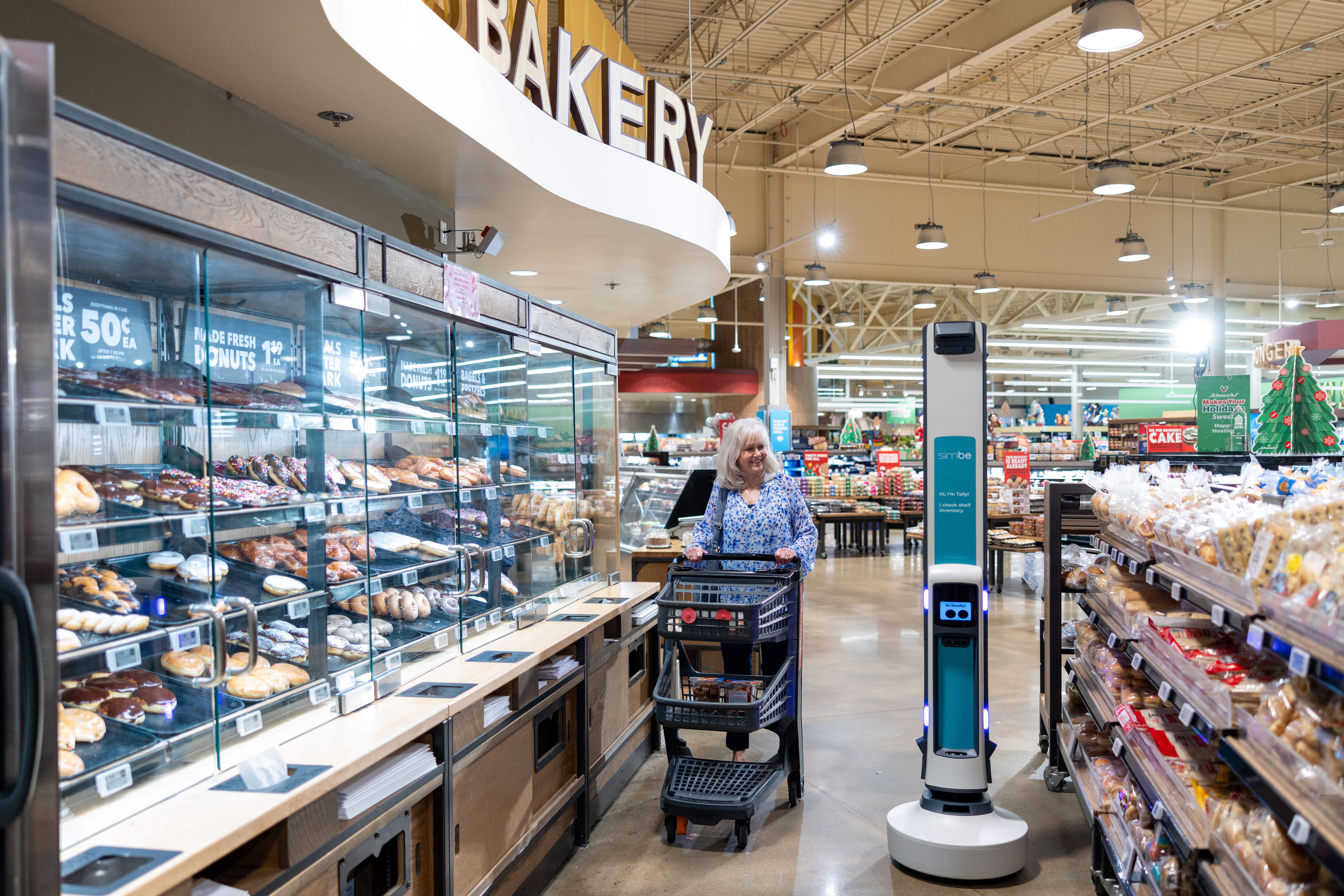 A shopper and a Tally robot pass in a supermarket bakery aisle