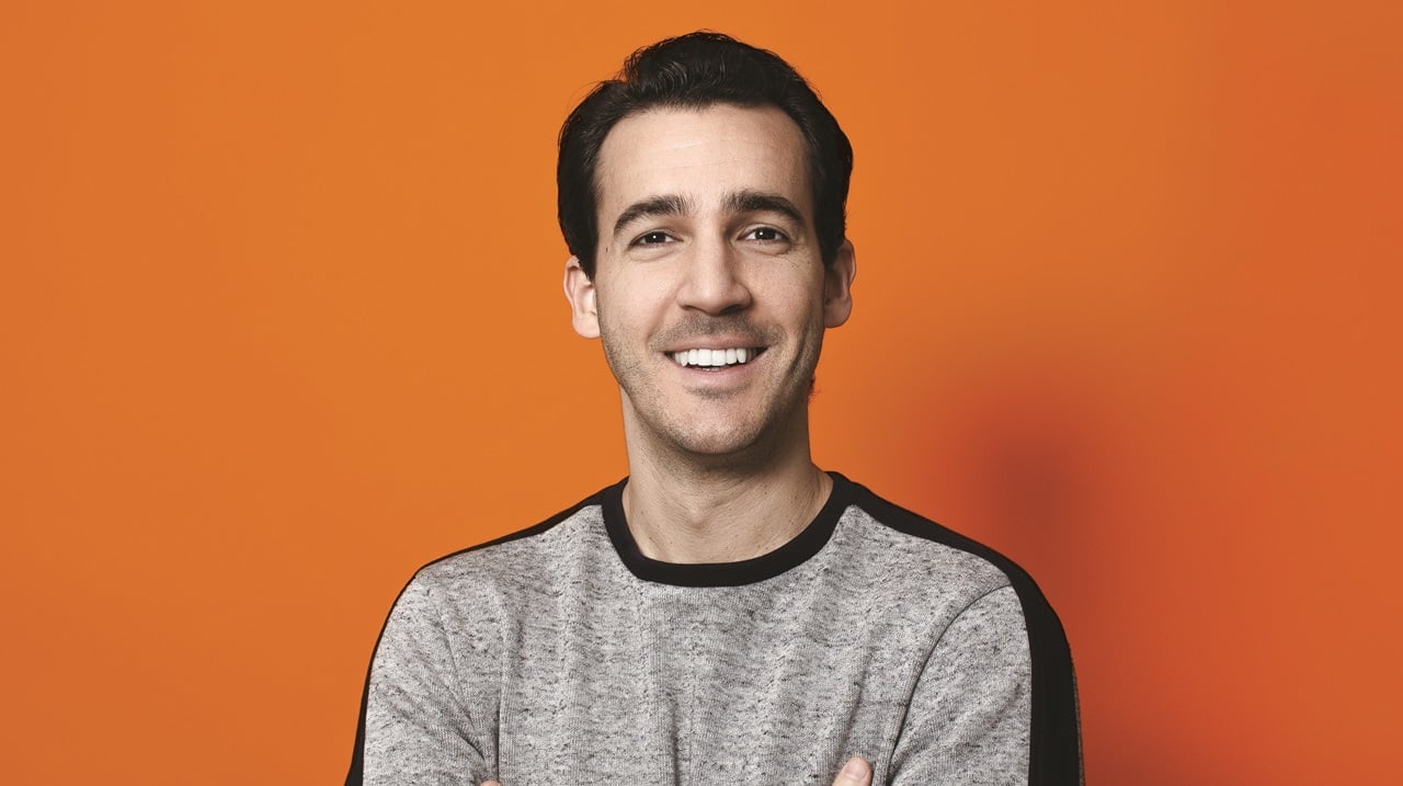 Simón Borrero smiles with his arms crossed against an orange backdrop