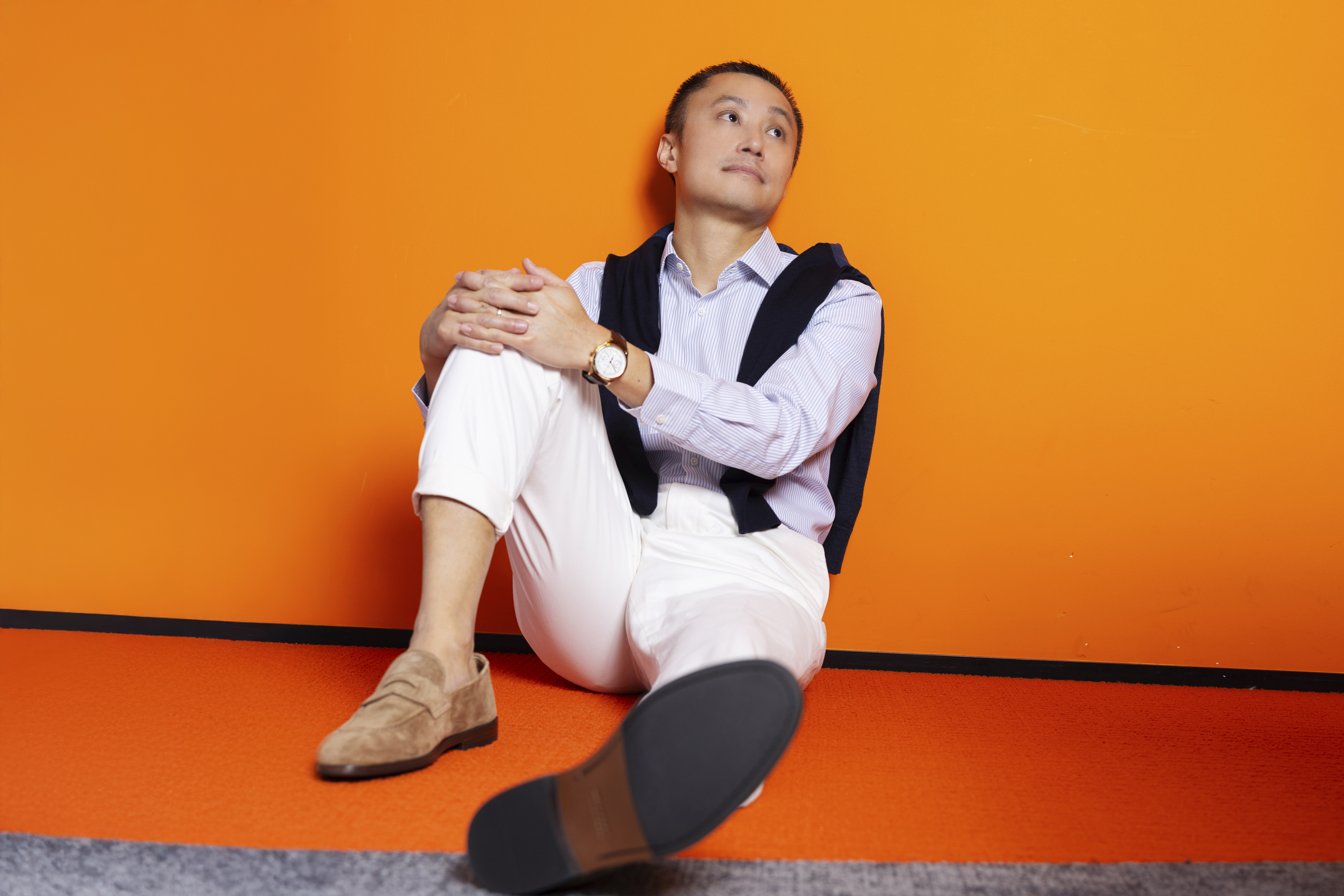 Simon Loong seated against an orange wall during a magazine photoshoot at the WeLab office