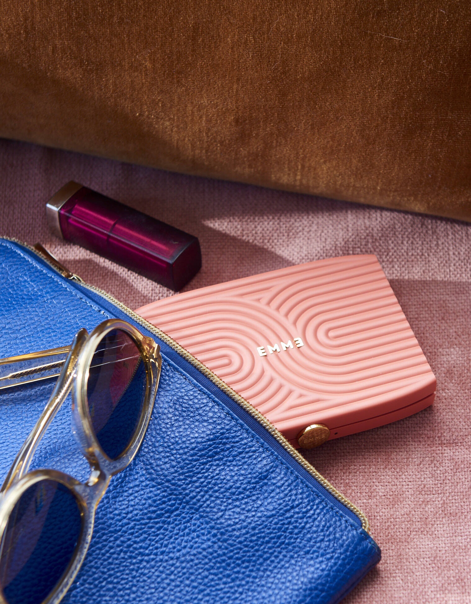 Pink Emme smart pill case tucked into a blue pouch beside sunglasses and lipstick