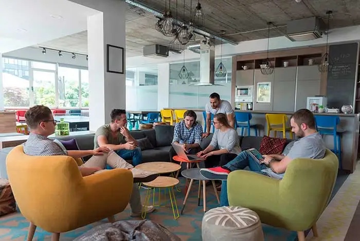 People discussing work around a laptop in a colorful office lounge, in a photograph published by Simplus