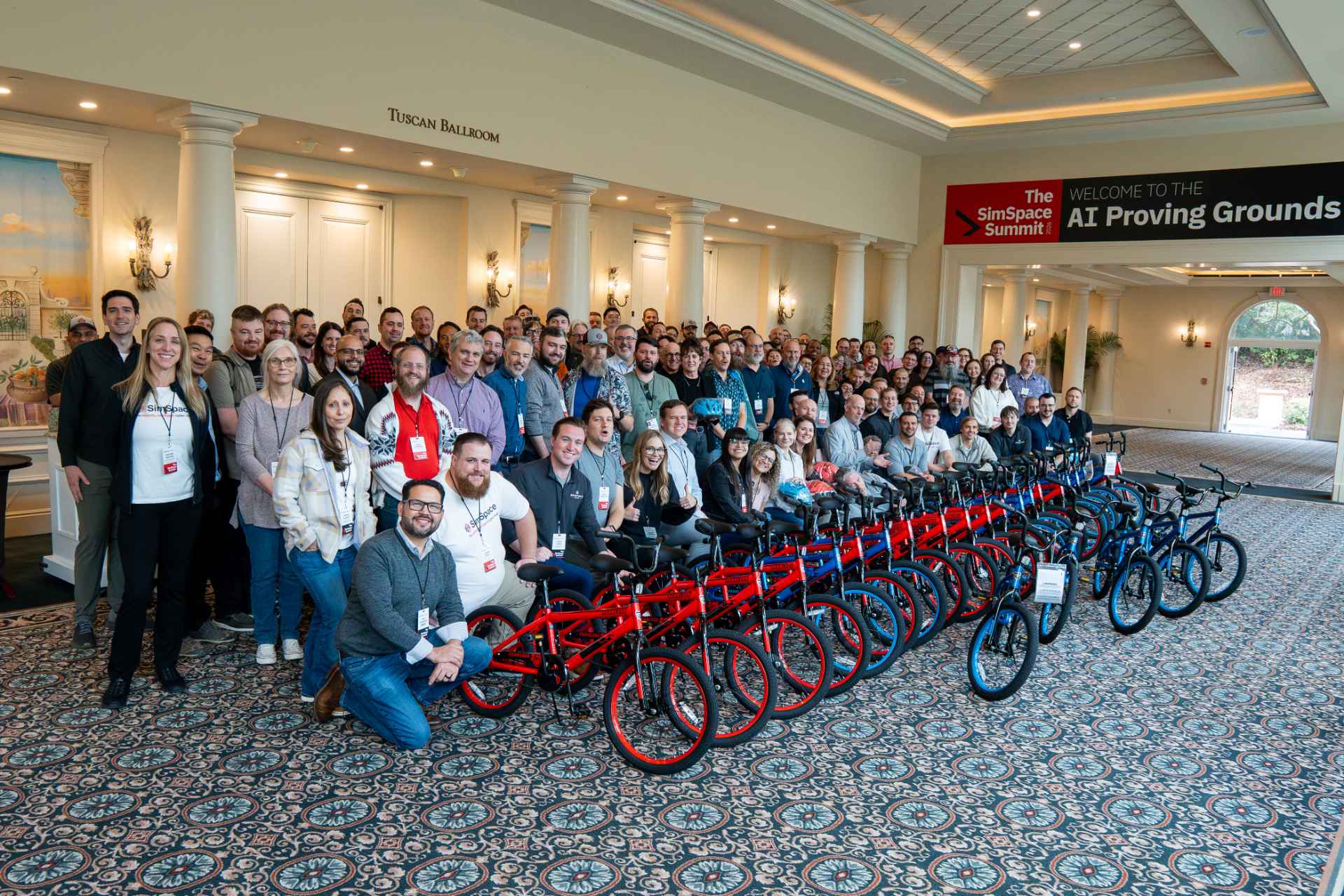 A large SimSpace Summit group gathered behind rows of red bicycles at the AI Proving Grounds event
