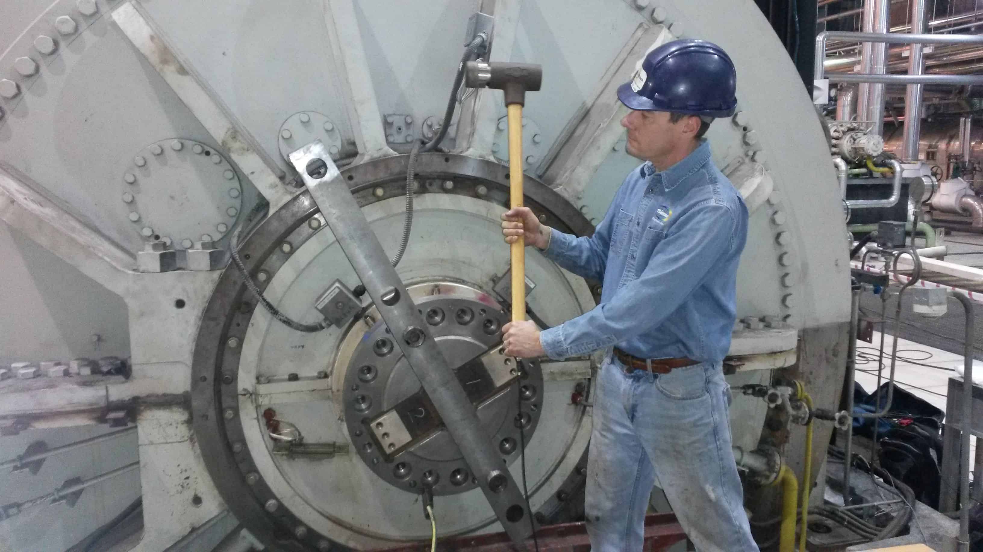 Test engineer holding a hammer beside a large generator during vibration testing