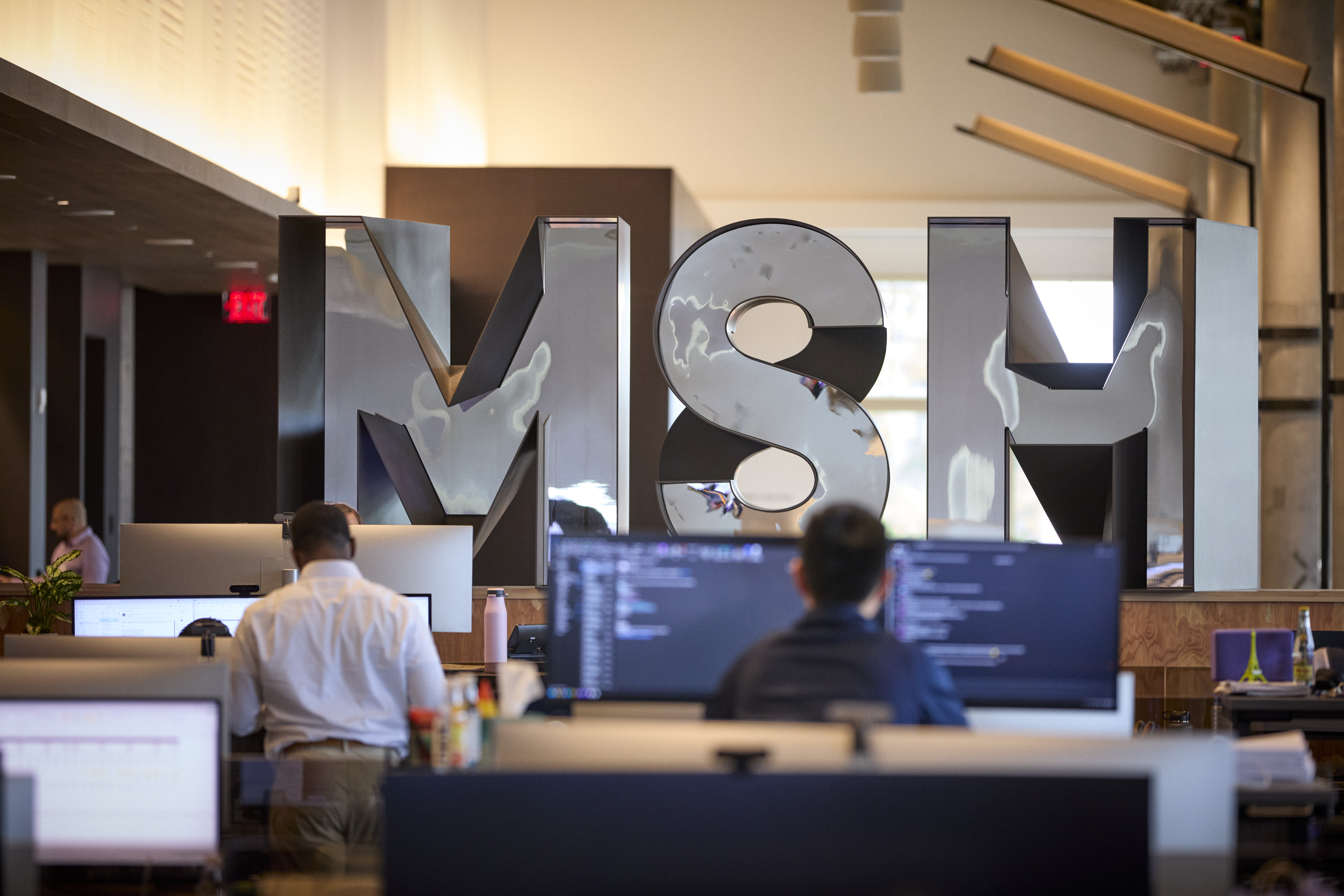 Employees at desks beneath large mirrored MSH letters in Sixth Street’s San Francisco office