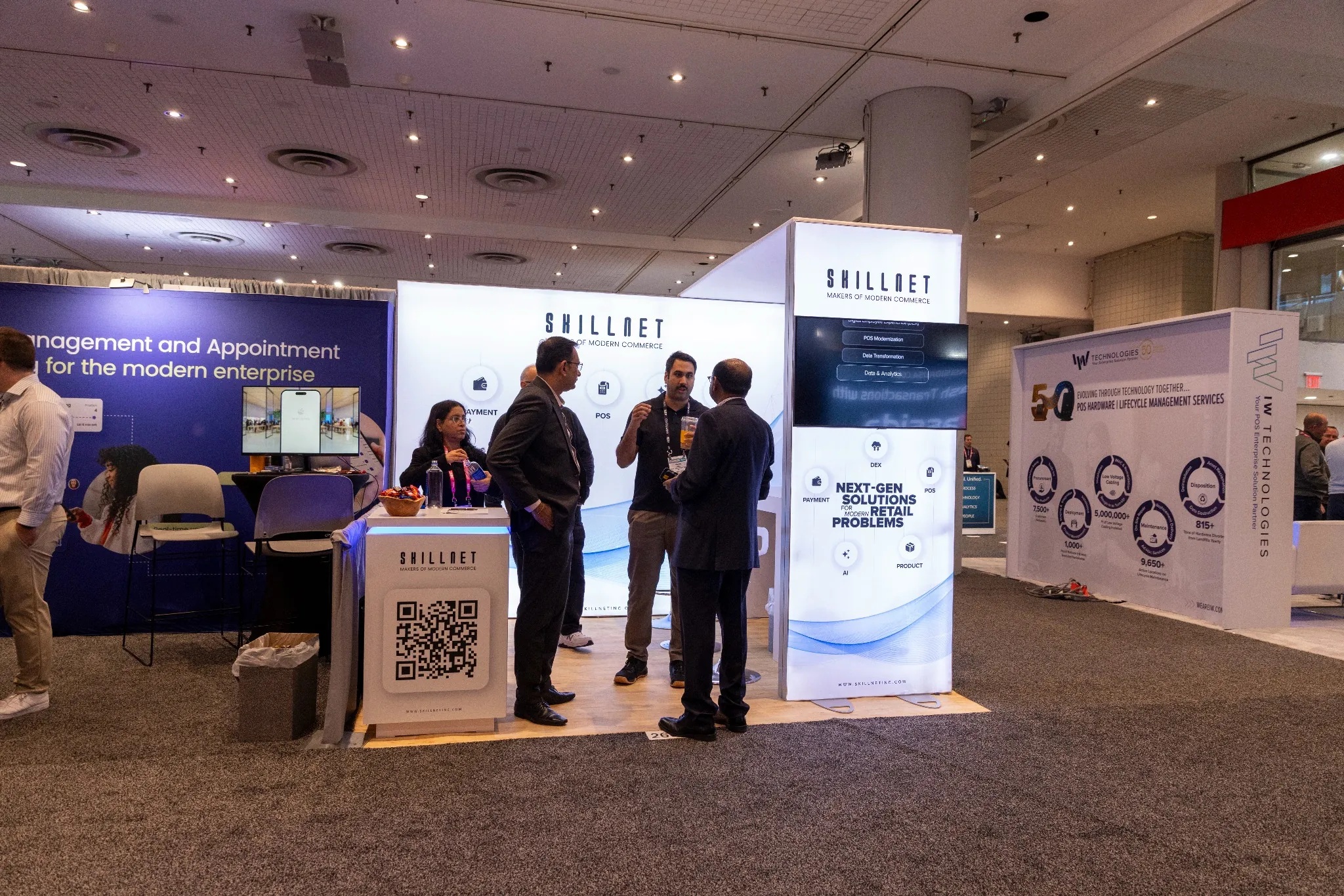 Attendees talking at SkillNet’s illuminated exhibition booth at NRF 2026