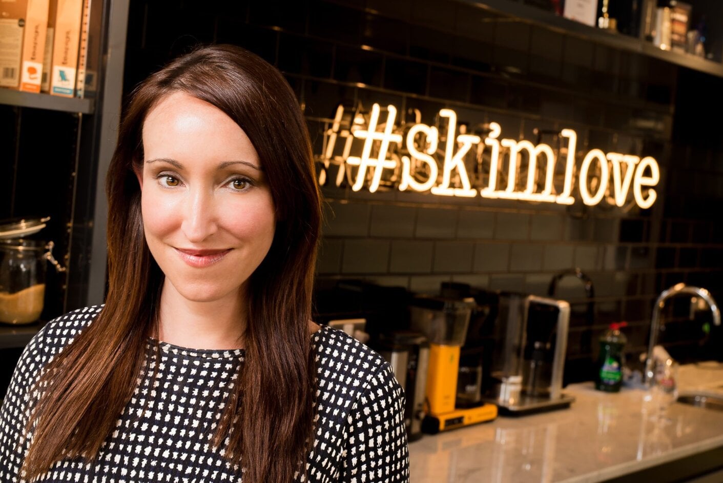 Skimlinks co-founder Alicia Navarro in an office kitchen beside a neon #skimlove sign