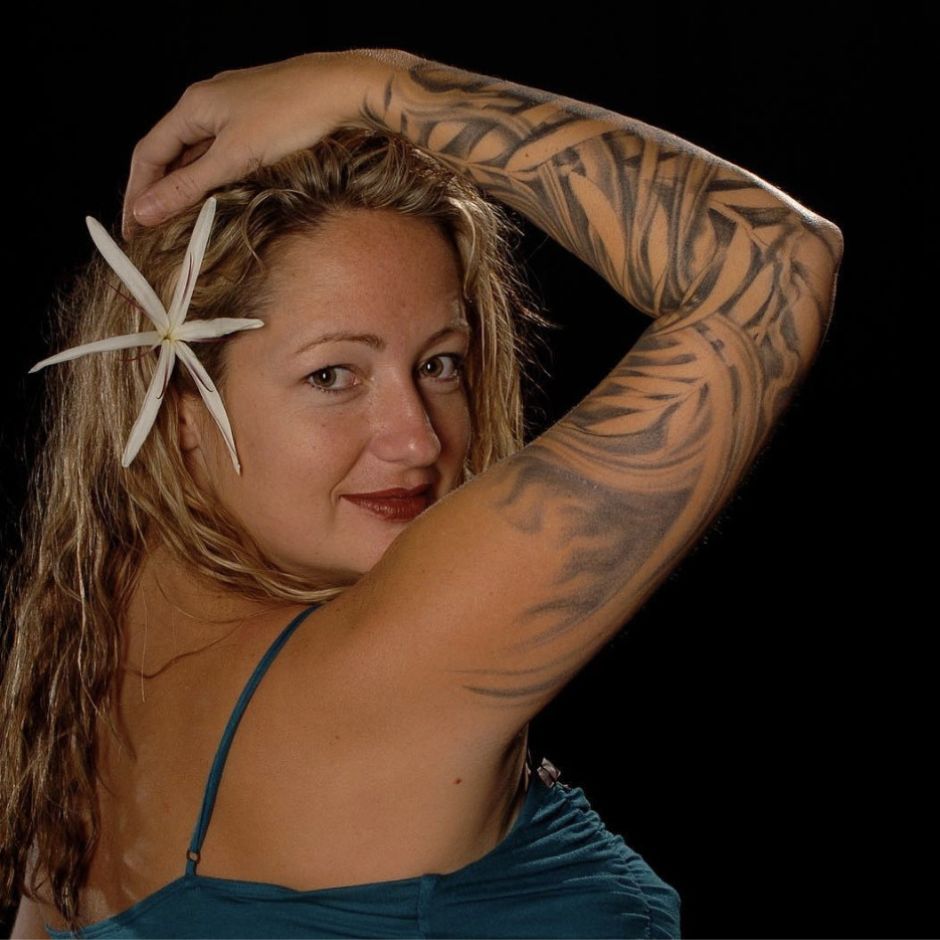 Skin Deep artist Anna Paige posing with her tattooed arm raised and a flower in her hair