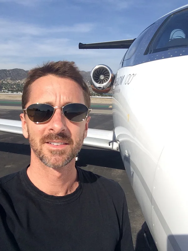 Sky Dayton wearing sunglasses beside a small jet on an airfield