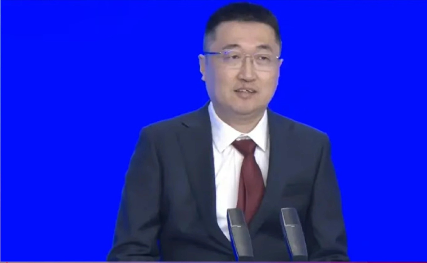 Sky Xu wearing glasses, a dark suit and a burgundy tie, speaking at the Guangdong development conference