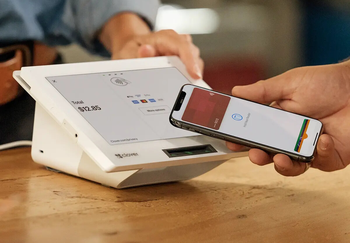 A customer holding a smartphone over a Clover contactless payment terminal
