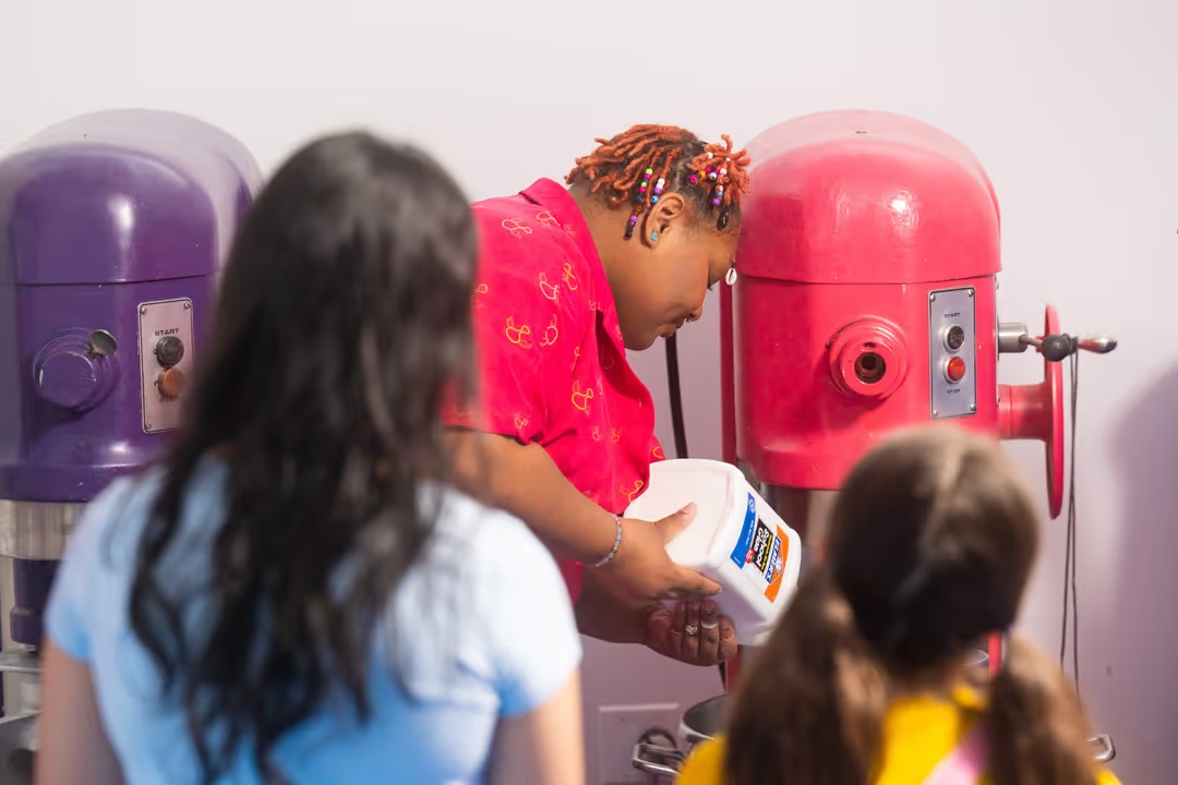 Visitors watch glue being handled beside large mixers in the Sloomoo slime kitchen