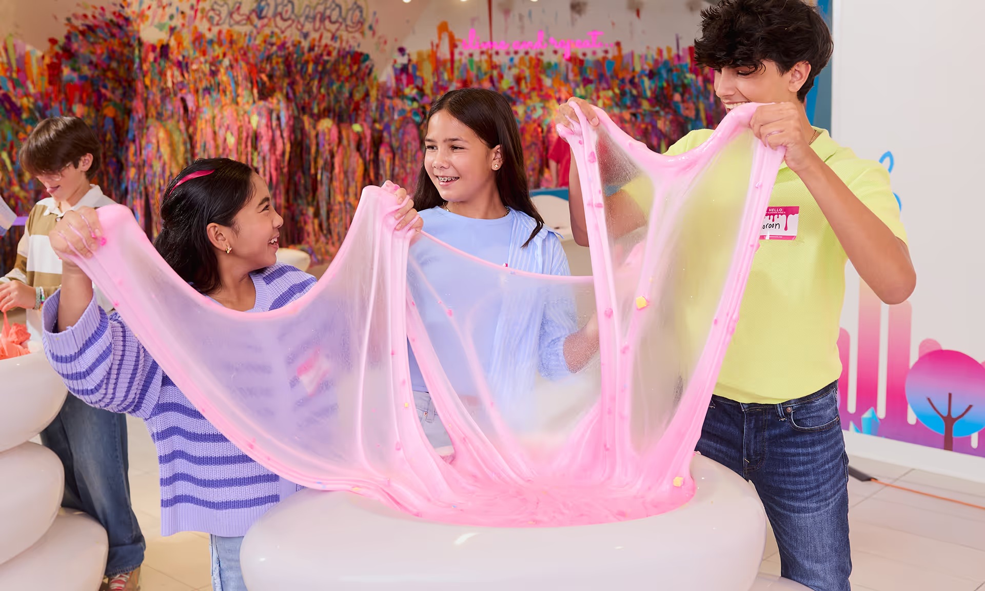 Three children stretch a sheet of pink slime together at Sloomoo