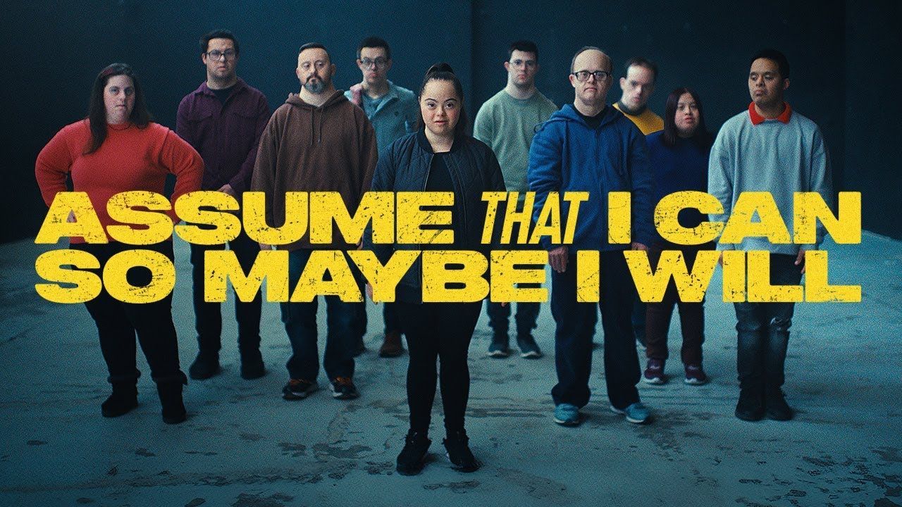 The Assume That I Can campaign ensemble beneath its yellow campaign lettering