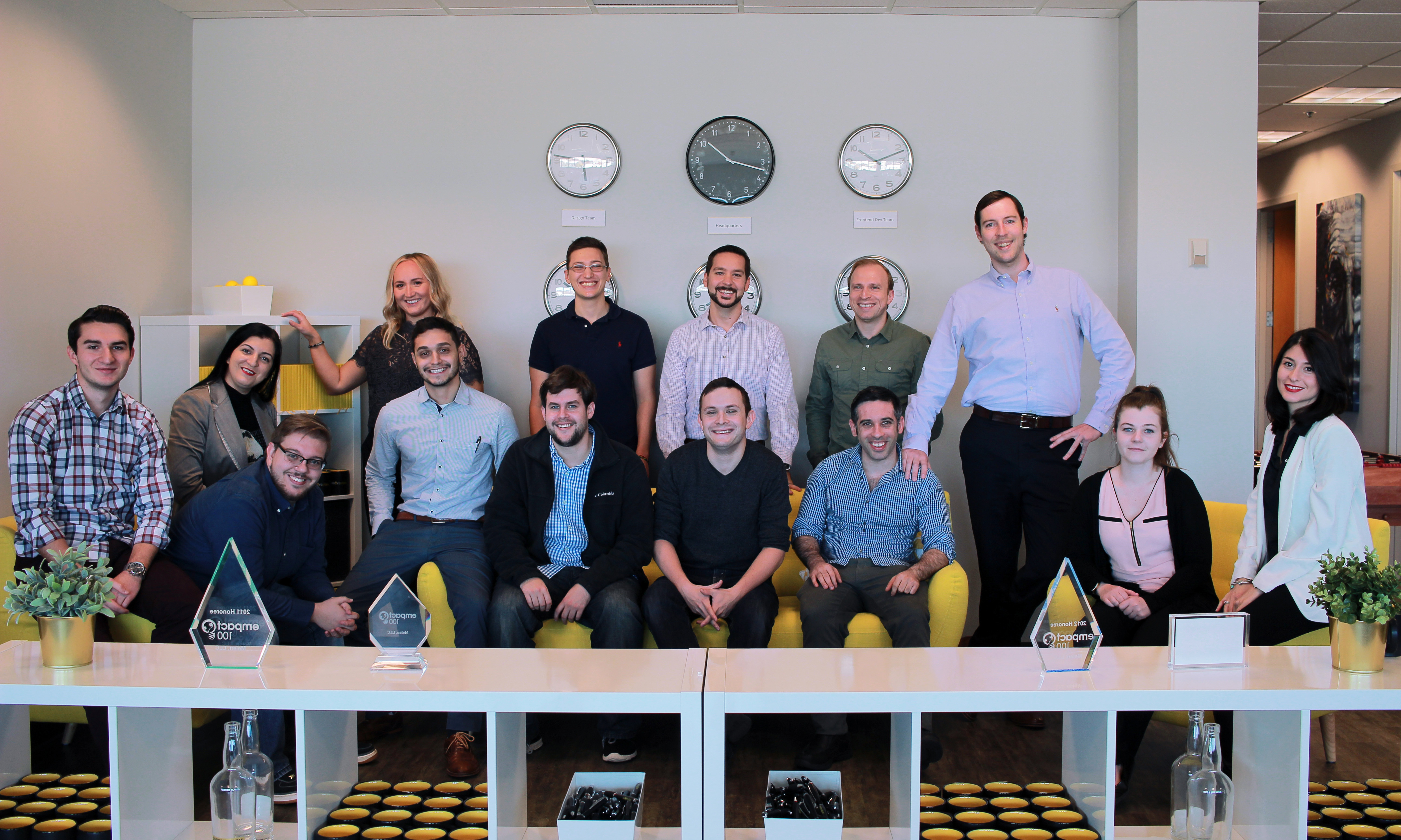 SmartSites team gathered around yellow sofas and a table of awards in an office