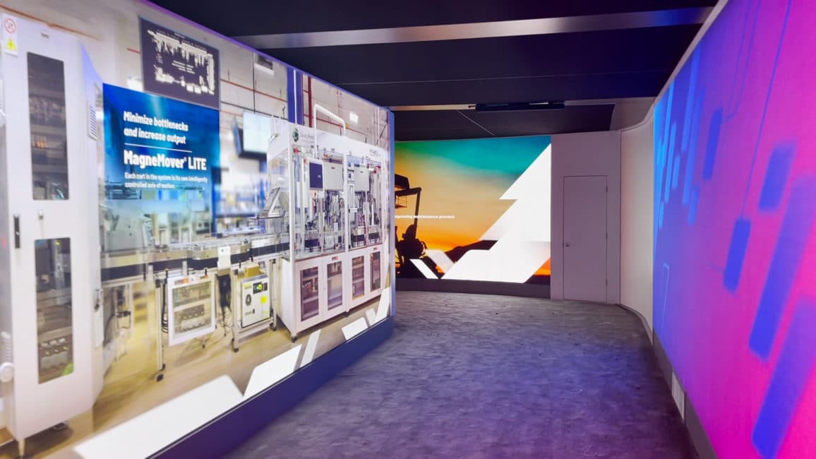Curved LED display walls showing manufacturing imagery around a carpeted walkway